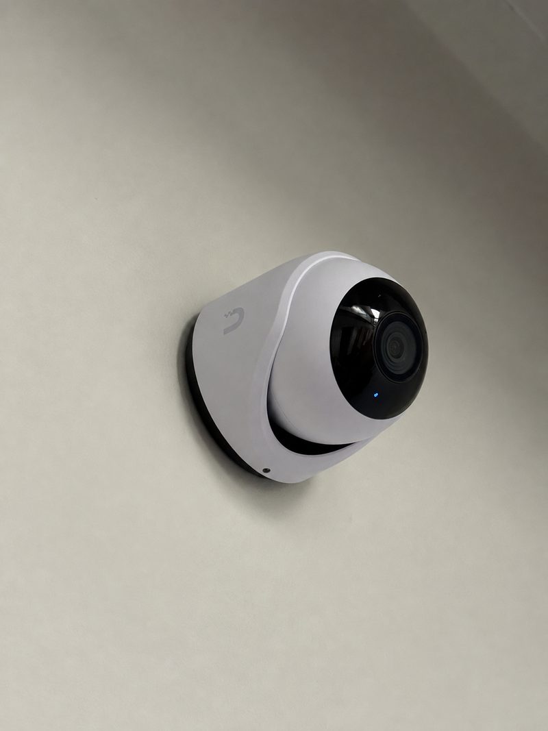 A white dome security camera mounted on a plain wall, angled toward the room.
